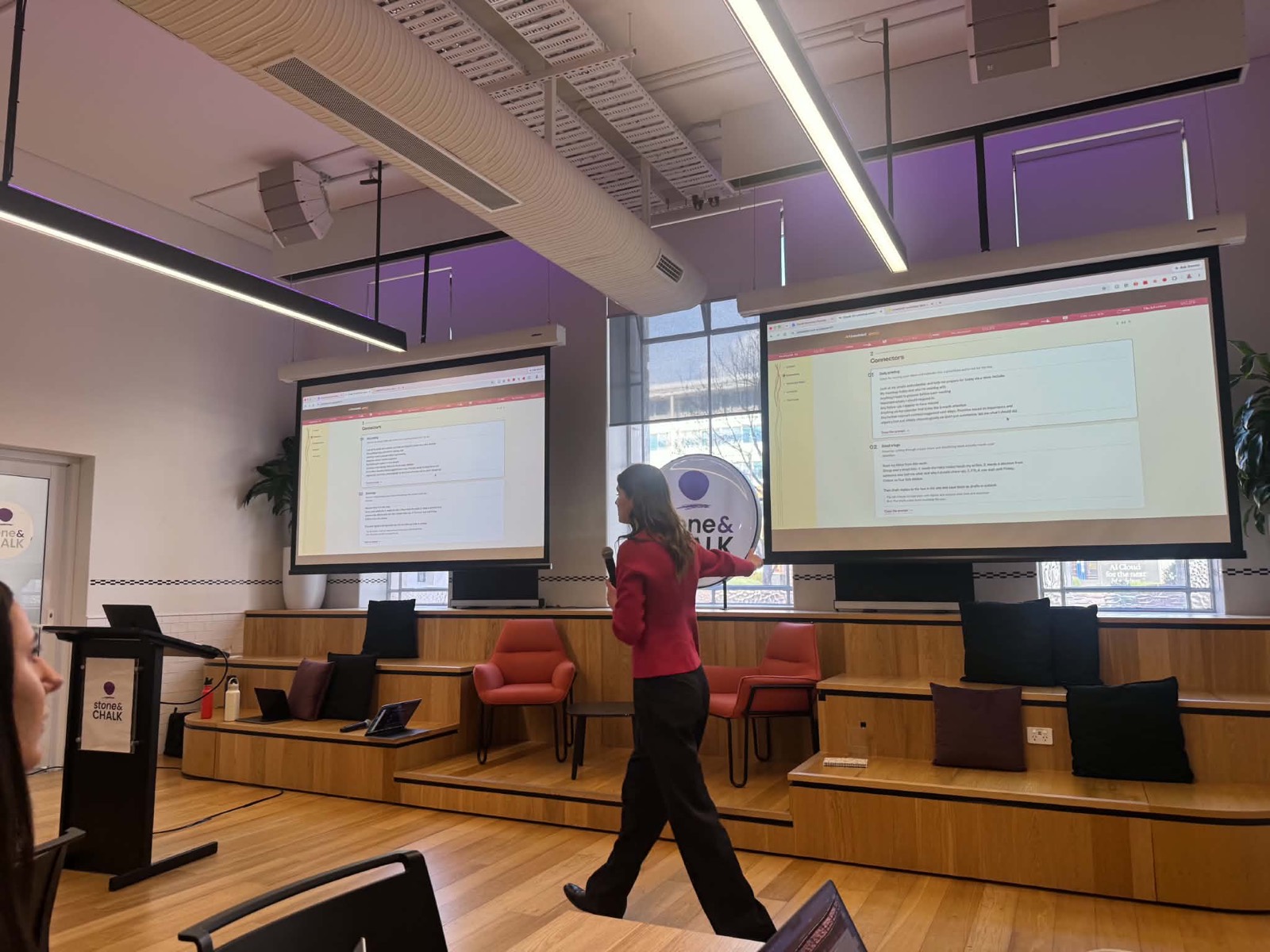 Jess Tresidder speaking with a microphone in front of two projector screens showing Claude connectors.